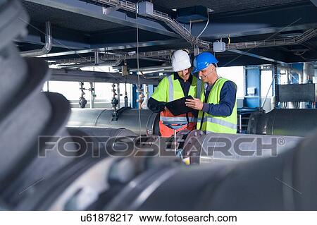 Stock Photo - Engineers reading digital tablet at geothermal power station. Fotosearch