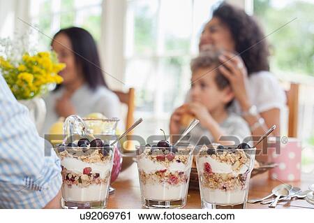 Stock Image - "Family enjoying meal together, focus on desserts in foreground". Fotosearch