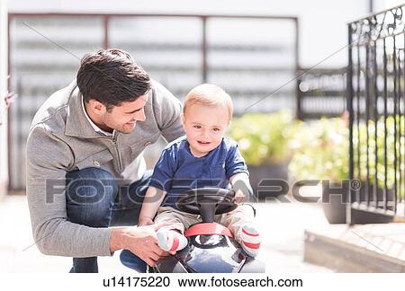 Stock Image - "Father and and young son playing together, son riding toy car". Fotosearch