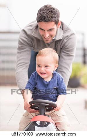 Stock Photo - "Father and and young son playing together, son riding toy car". Fotosearch