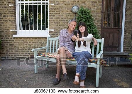"Father and daughter, sitting on bench, taking self portrait, using smartphone" View Large Photo Image Stock Image - "Father and daughter, sitting on bench, taking self portrait, using smartphone". Fotosearch