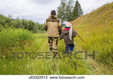 Stock Image - "Father and son walking through field, carrying fishing net, rear view". Fotosearch