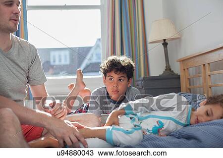 Stock Image - Father and two sons relaxing on bed. Fotosearch