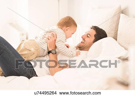 Picture - "Father and young son relaxing together on bed, laughing". Fotosearch