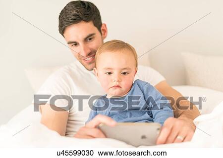 "Father and young son sitting together, looking at smartphone" View Large Photo Image Stock Image - "Father and young son sitting together, looking at smartphone". Fotosearch