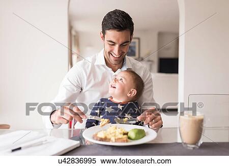 Stock Photography - Father eating meal with young son sitting on his lap. Fotosearch