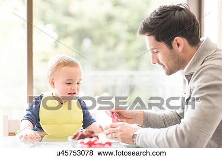 Stock Photo - "Father feeding young son, indoors". Fotosearch