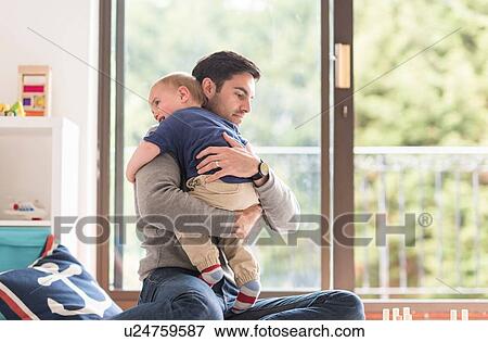 Stock Photo - "Father hugging young son, indoors". Fotosearch