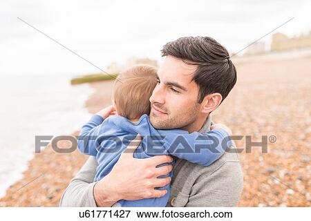 Stock Photo - Father hugging young son on pebble beach. Fotosearch