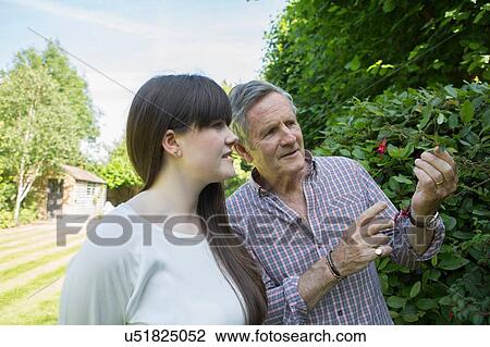 Stock Image - Father looking at flowers in garden with grown daughter. Fotosearch