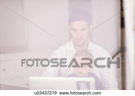 "Father using laptop while young son sits on his lap, taken through window" View Large Photo Image Stock Photo - "Father using laptop while young son sits on his lap, taken through window". Fotosearch