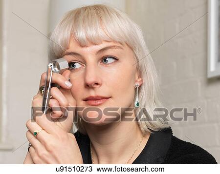 Stock Image - Female jeweler examining diamond using magnifier in jewellery shop. Fotosearch
