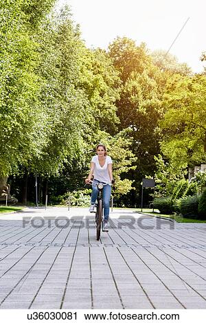 Stock Image - "Front view of young woman riding bicycle, looking at camera". Fotosearch