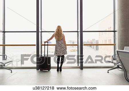 Full length rear view of woman standing holding suitcase looking out of window View Large Photo Image Stock Photo - Full length rear view of woman standing holding suitcase looking out of window. Fotosearch