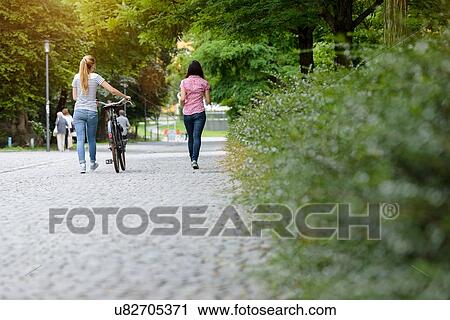 Stock Image - Full length rear view of women walking with bicycle. Fotosearch
