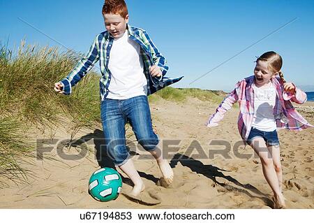 "Girl and boy chasing football across sand, smiling" View Large Photo Image Stock Image - "Girl and boy chasing football across sand, smiling". Fotosearch