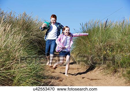 Girl and boy running through marram grass holding football smiling View Large Photo Image Stock Image - Girl and boy running through marram grass holding football smiling. Fotosearch