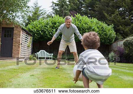 Stock Image - Grandfather and grandson playing with football in garden. Fotosearch