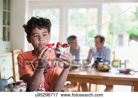 Stock Photo - "Grandson holding breakfast granola, father and grandfather sitting behind at kitchen table". Fotosearch