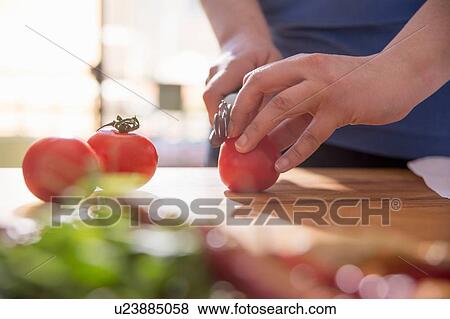 Stock Photo - Hands of woman slicing tomato at kitchen counter. Fotosearch