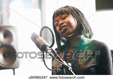 Head and shoulders of young woman singing into microphgone through pop guard View Large Photo Image Stock Photo - Head and shoulders of young woman singing into microphgone through pop guard. Fotosearch