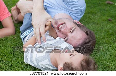 High angle view of father and son lying on grass playfighting and laughing View Large Photo Image Stock Image - High angle view of father and son lying on grass playfighting and laughing. Fotosearch