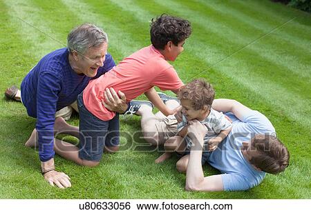 Stock Photograph - High angle view of three generation family on grass playfighting. Fotosearch