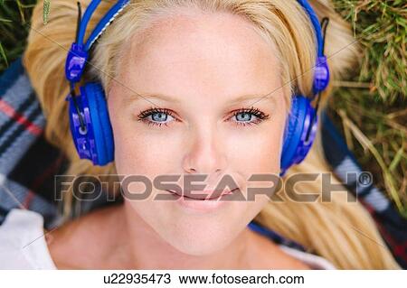 High angle view of young woman wearing headphones lying on blanket looking at camera smiling View Large Photo Image Stock Image - High angle view of young woman wearing headphones lying on blanket looking at camera smiling. Fotosearch