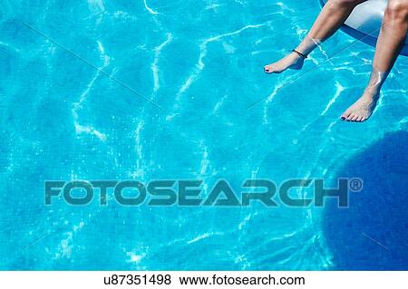 Stock Photo - Legs and feet of teenage girl dangling in swimming pool. Fotosearch