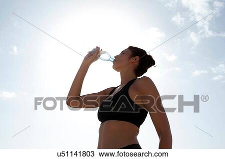 Low angle view of blue sky and mid adult woman drinking bottled water View Large Photo Image Stock Image - Low angle view of blue sky and mid adult woman drinking bottled water. Fotosearch