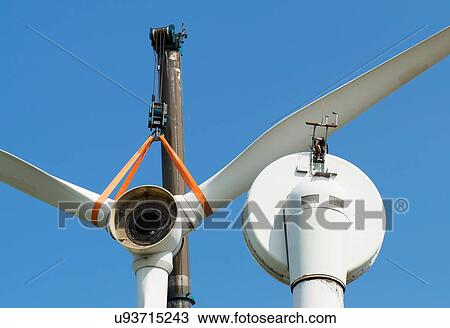 Stock Image - Low angle view of wind turbine being dismantled by worker. Fotosearch