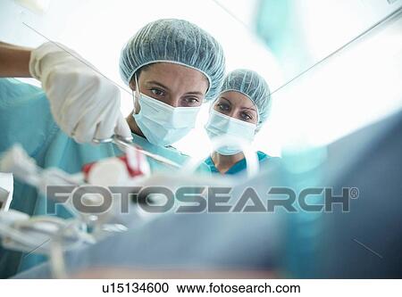 Stock Image - Male and female surgeons concentrating in hospital operating theatre. Fotosearch