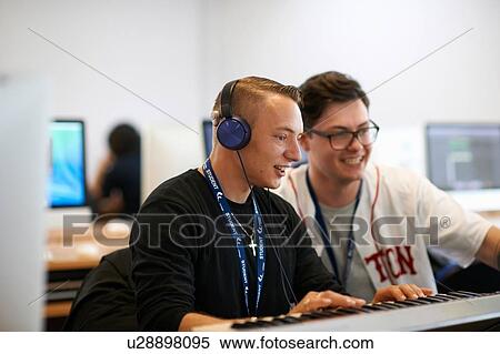 Stock Photography - Male college student wearing headphones playing keyboards looking away smiling. Fotosearch