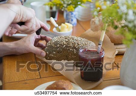Picture - "Man slicing granary bread in preparation for breakfast, focus on hands". Fotosearch