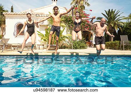 Stock Photo - Mature couple holding hands with son and daughter jumping into in swimming pool. Fotosearch