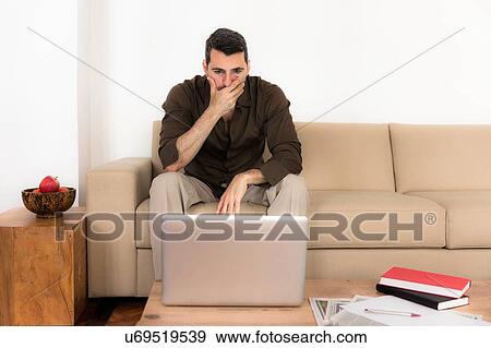 "Mature man sitting on sofa looking at laptop, hand over mouth" View Large Photo Image Stock Photo - "Mature man sitting on sofa looking at laptop, hand over mouth". Fotosearch