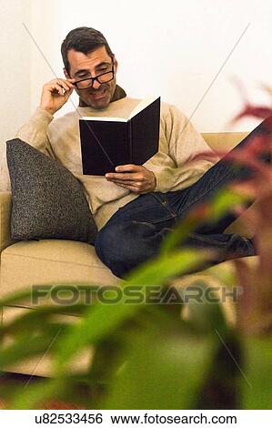 Mature man sitting on sofa wearing eye glasses reading a book View Large Photo Image Stock Photograph - Mature man sitting on sofa wearing eye glasses reading a book. Fotosearch