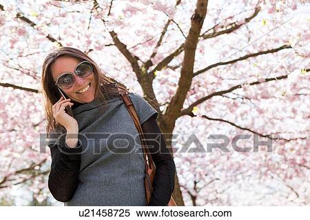 Stock Photography - Mature woman chatting on smartphone in front of cherry blossom. Fotosearch
