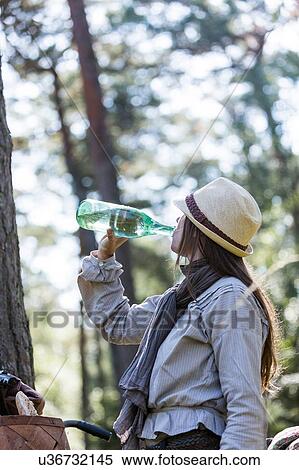 Stock Photography - Mature woman cyclist drinking from water bottle in forest. Fotosearch