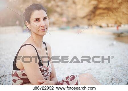 Stock Image - "Mature woman sitting on beach, Javea, Spain". Fotosearch