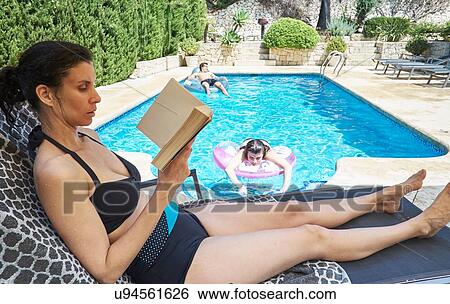 Mature woman sitting on poolside lounger reading book View Large Photo Image Stock Photograph - Mature woman sitting on poolside lounger reading book. Fotosearch