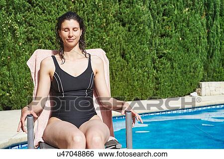 Stock Photograph - Mature woman wearing bathing costume sitting on poolside lounger. Fotosearch