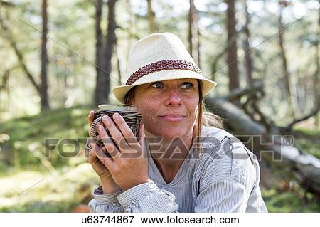 Mature woman wearing fedora drinking tea in forest View Large Photo Image Stock Photo - Mature woman wearing fedora drinking tea in forest. Fotosearch