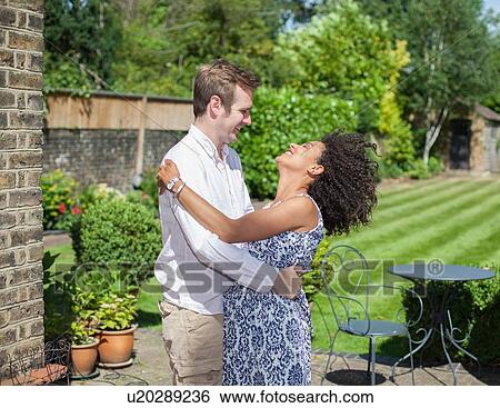 Stock Photograph - "Mid adult couple embracing, outdoors, laughing". Fotosearch