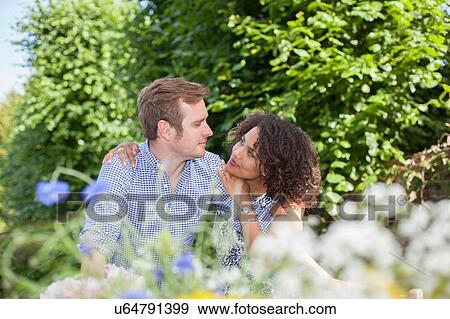 Stock Photo - "Mid adult couple, embracing, sitting face to face, outdoors". Fotosearch
