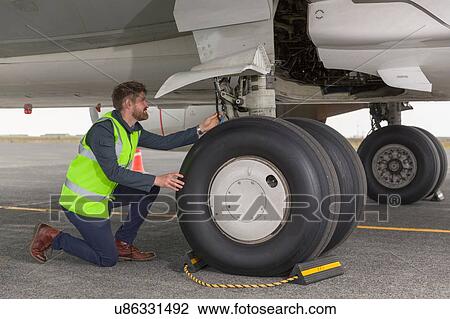 Mid adult man wearing high visability jacket kneeling down inspecting airplanes landing gear View Large Photo Image Stock Image - Mid adult man wearing high visability jacket kneeling down inspecting airplanes landing gear. Fotosearch