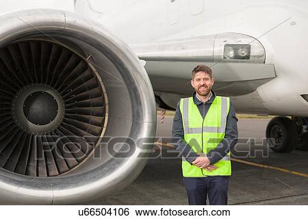 "Mid adult man wearing high visability jacket standing next to airplane engine, hands together, looking at camera smiling" View Large Photo Image Stock Photograph - "Mid adult man wearing high visability jacket standing next to airplane engine, hands together, looking at camera smiling". Fotosearch