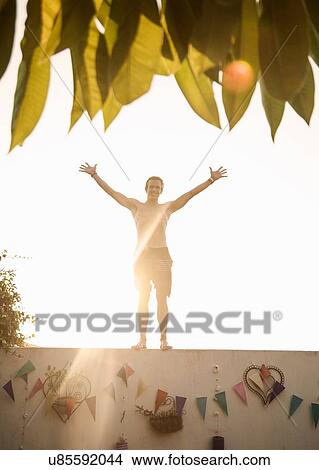 Picture - Mid adult man wearing swimming shorts standing on wall at poolside party. Fotosearch