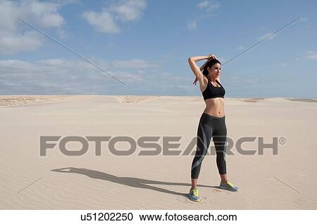 Stock Image - Mid adult woman exercising on beach. Fotosearch