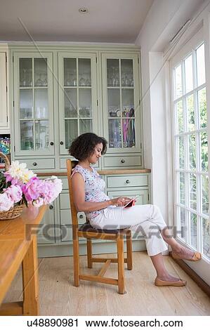Stock Image - "Mid adult woman in kitchen, looking at digital tablet". Fotosearch
